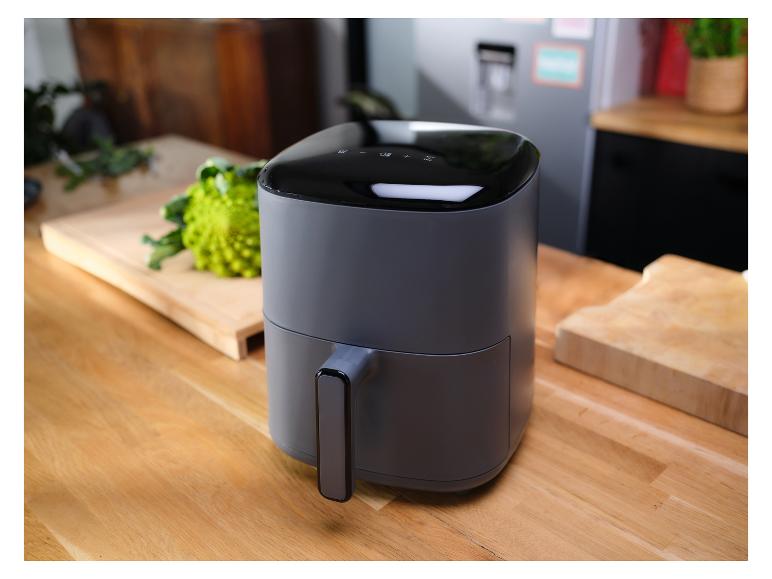 Eine graue Heißluftfritteuse auf einer Holzküchenarbeitsplatte, mit Gemüse im Hintergrund.