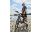 Mann auf einem Fahrrad am Wasser mit einer Trinkflasche in der Hand.