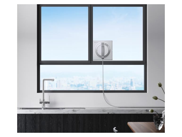 Fensterputzroboter an einem großen Fenster mit Stadtblick, über einer Küchenspüle.