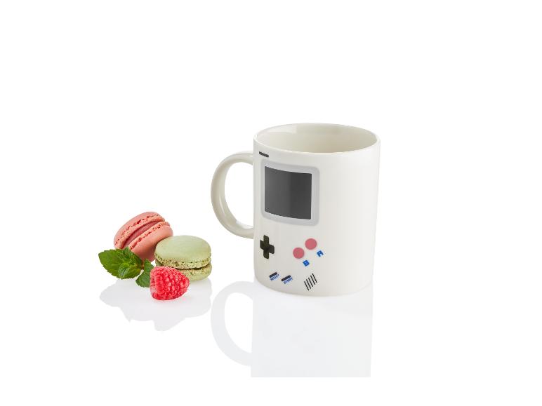Eine Tasse mit Gamepad-Design, zwei Macarons und eine Himbeere.
