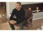 Mann in schwarzem Langarmshirt und grüner Hose sitzt auf einem Ledersessel.