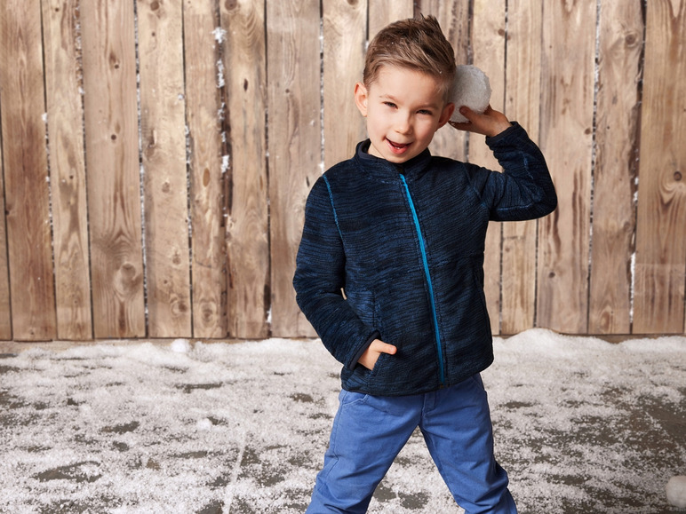 Ein kleiner Junge in einer blauen Jacke und blauen Hosen hält eine Schneeball.