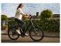 Junge Frau in Jeansjacke und dunklen Jeans fährt mit einem E-Bike eine Wohnstraße entlang.