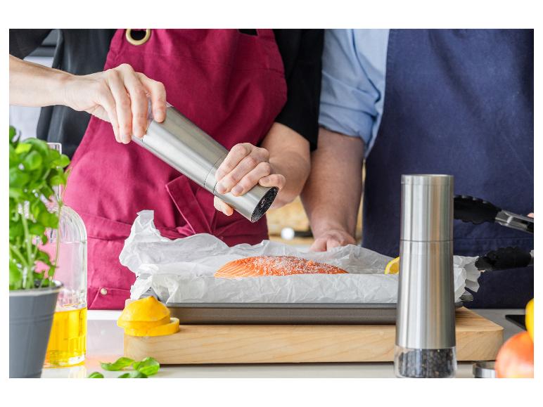 Zwei Personen bereiten Lachs zu, fügen Salz und Pfeffer hinzu.