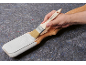 Hand streicht ein Holzbrett weiß auf grauem Filzuntergrund.