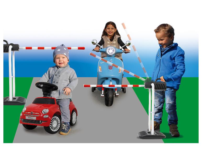 Kinder spielen mit Kinderautos und -rollern auf einem Spielplatz mit Schranke.