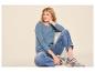 Frau in blauem Langarmshirt, Jeans und Turnschuhen, auf dem Boden sitzend.