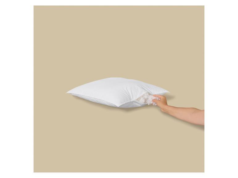 Weißes Kissen mit offenem Reißverschluss, aus dem die Füllung entnommen wird.