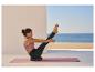 Frau macht Yoga auf einer Yogamatte und einem Balancekissen am Meer.