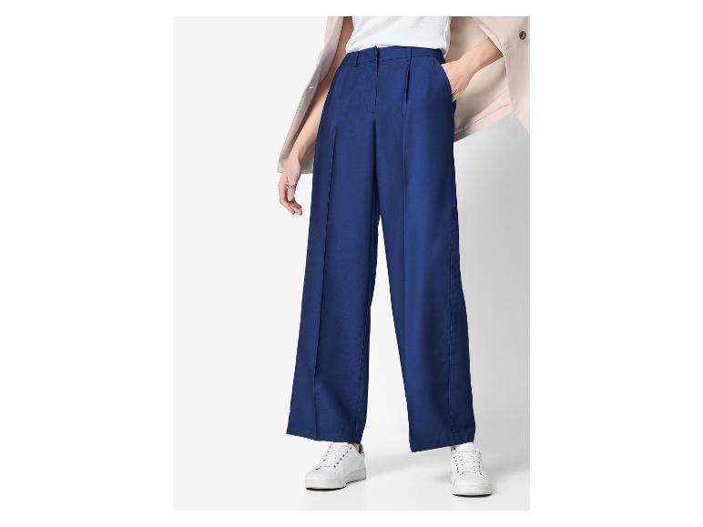 Marineblaue weite Hose mit Falten, weißes Oberteil und beigefarbene Jacke.