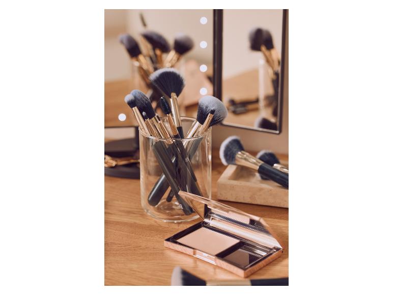 Make-up-Pinsel in einem Glasbehälter und ein Kompaktpuder auf einem Schminktisch aus Holz.