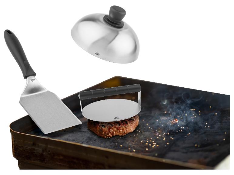 Metallspatel, Burgerpresse und Kuppeldeckel auf einem grillenden Burger