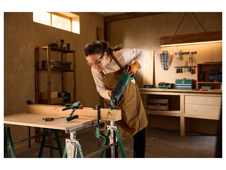 Frau in einer Werkstatt sägt einen Holzbalken mit der PARKSIDE Säbelsäge PFS 850 C3.