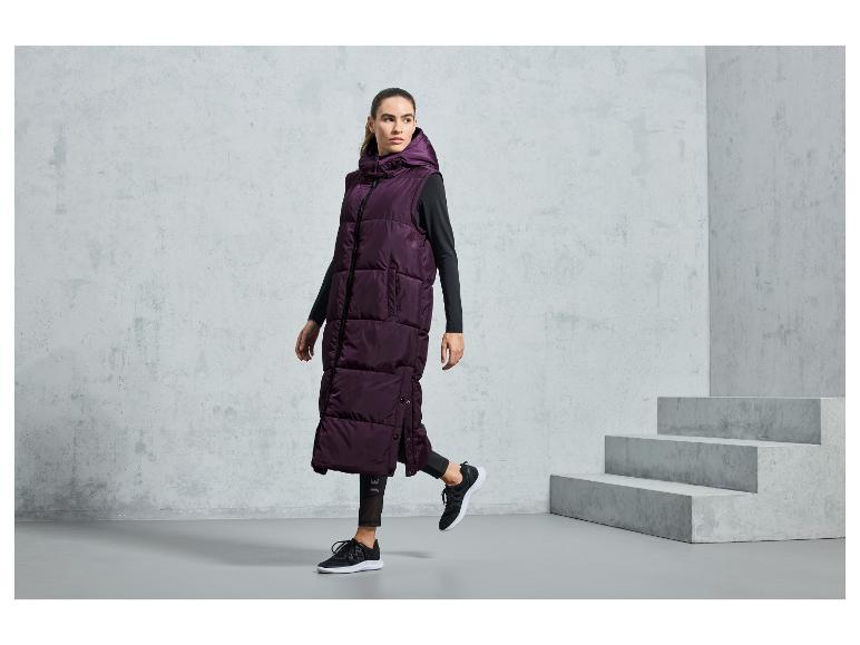 Eine Frau trägt eine lange, violette Steppweste und schwarze Sportschuhe.