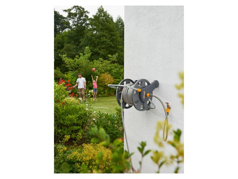 Wandschlauchaufroller mit Gartenschlauch, Mann bewässert Garten, Mädchen spielt mit Ball.