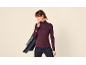 Frau in pflaumenfarbenem Rollkragenpullover, dunklen Jeans und Jeanshemd über der Schulter.