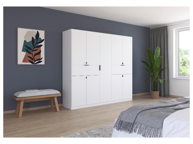 Ein weißer Kleiderschrank mit sechs Türen und ein Bett mit einer grauen Bettdecke in einem modernen Schlafzimmer.