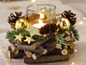 Eine Weihnachtskerze in einem Glas, umgeben von Ästen, Zapfen und goldenen Weihnachtskugeln.