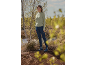 Frau in grünem Pullover, dunkelblauen Jeans und blauen Stiefeln in der Natur.