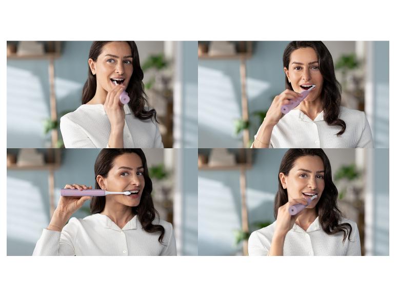 Eine Frau lächelt, während sie sich die Zähne mit einer lila elektrischen Zahnbürste putzt.