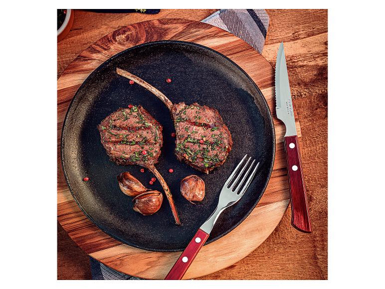Zwei gegrillte Lammkoteletts mit Knoblauch und Besteck auf einem Holzbrett.