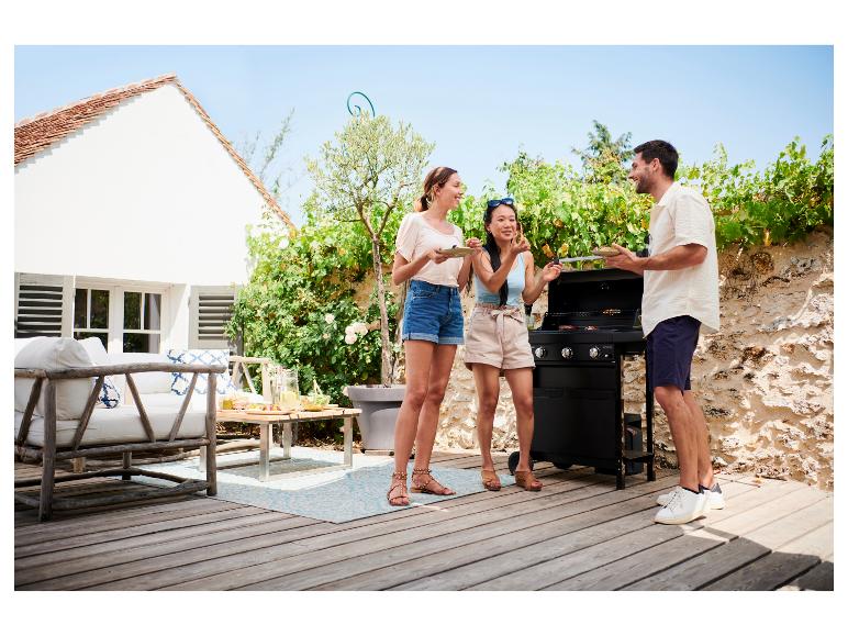 Drei Freunde grillen draußen auf einer Terrasse mit Gartenmöbeln.
