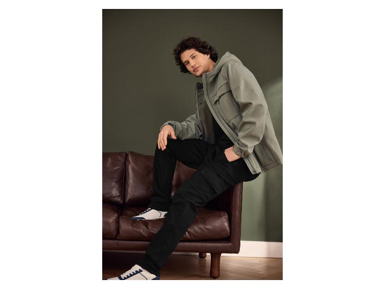Mann in grüner Jacke und schwarzer Hose sitzt auf einem braunen Sofa.