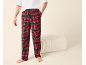 Mann in roter karierter Pyjamahose und weißem T-Shirt, neben einem beigen Hocker stehend.