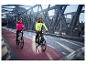 Zwei Radfahrer in CRIVIT Thermo-Hybridjacken auf einer Brücke, eine in Pink, eine in Neongelb.