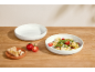 Zwei weiße Schalen, eine gefüllt mit Nudelsalat, die andere leer, mit Tomaten und Käse.