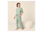 Frau in hellgrünem Pyjama-Set mit Hose und T-Shirt, stehend neben einem Pouf.