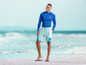 Mann in blauem Rashguard und blauen Shorts mit 'mi' Logo am Strand.