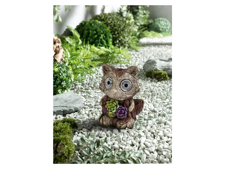 Eine solarbetriebene Gartenleuchte in Form eines Waschbären in einem Kiesgarten.