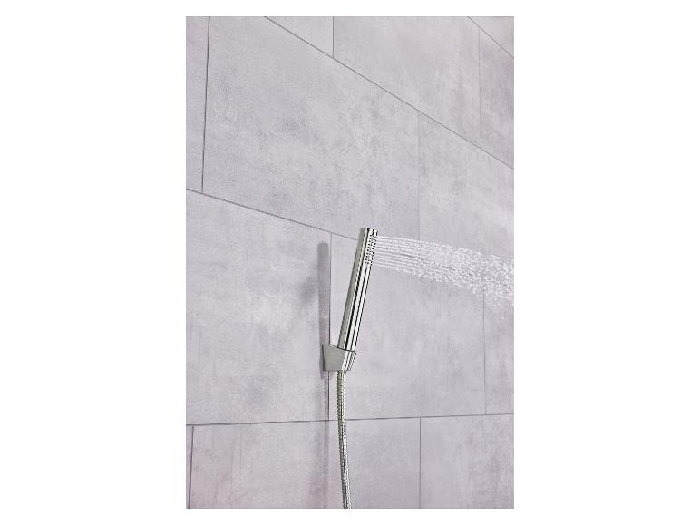 Verchromter Duschkopf sprüht Wasser an eine hellgraue Fliesenwand.