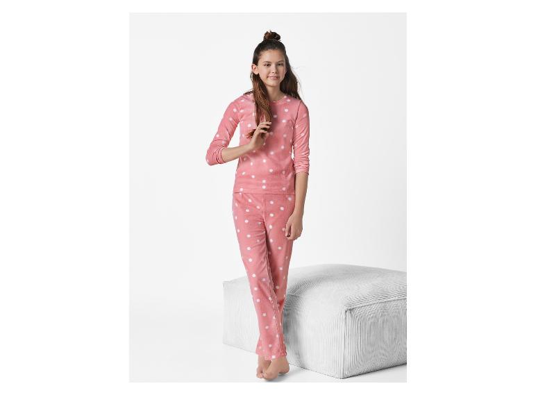 Mädchen in rosa Pyjama mit weißen Punkten, neben einem weißen Hocker.