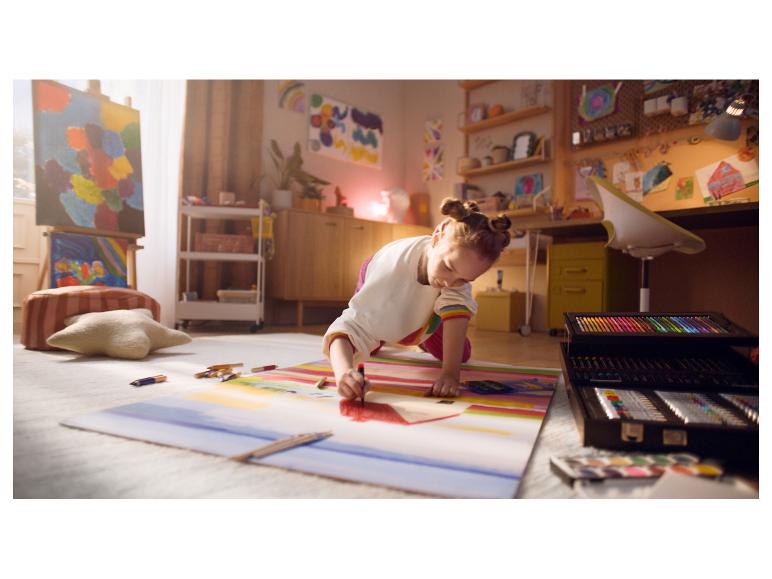 Ein Mädchen zeichnet auf dem Boden mit einem großen Kunstset in einem Raum voller Kunst.