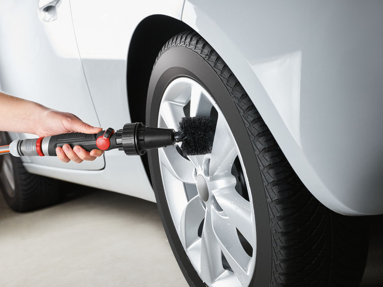 Eine Hand wäscht ein Autoreifen mit einer Bürste an einem Schlauch.
