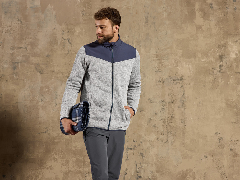 Mann in einem grauen Fleece-Jackett mit einer blauen karierten Decke.