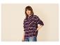 Frau in bordeauxrotem Karoshirt und Jeans, mit der Hand in der Hüfte.