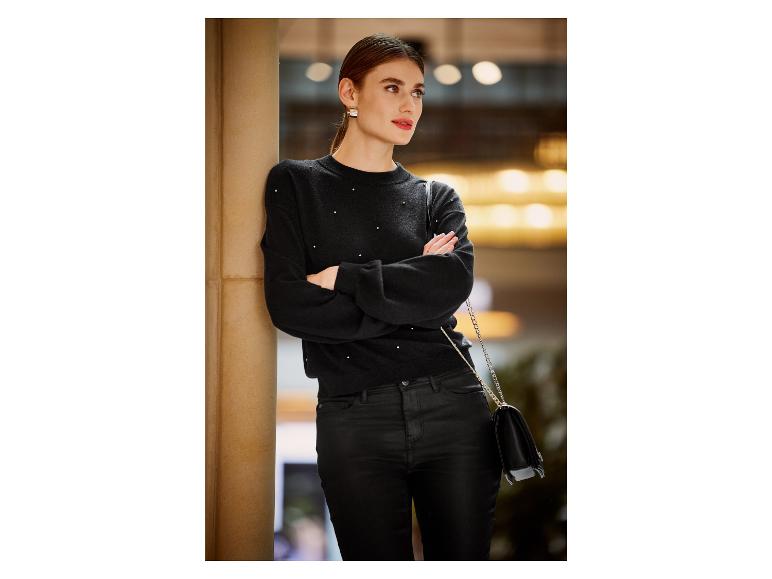 Eine Frau trägt einen schwarzen Pullover mit Perlen und eine schwarze Lederhandtasche.
