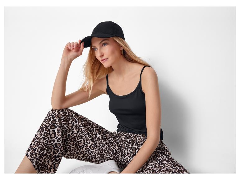 Eine Frau in schwarzem Tanktop, Leopardenhose und schwarzer Baseballkappe.