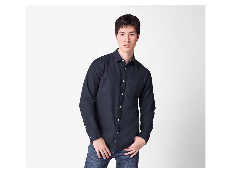 Ein Mann in einem dunkelblauen Hemd und Jeans steht mit den Händen in den Taschen.