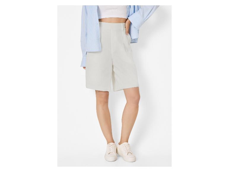 Frau in hellgrauen Shorts, weißem Crop-Top, blau gestreiftem Hemd und weißen Sneakern.