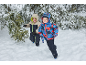 Zwei Jungen in Winteroveralls und Jacken rennen im Schnee neben Tannenbäumen.