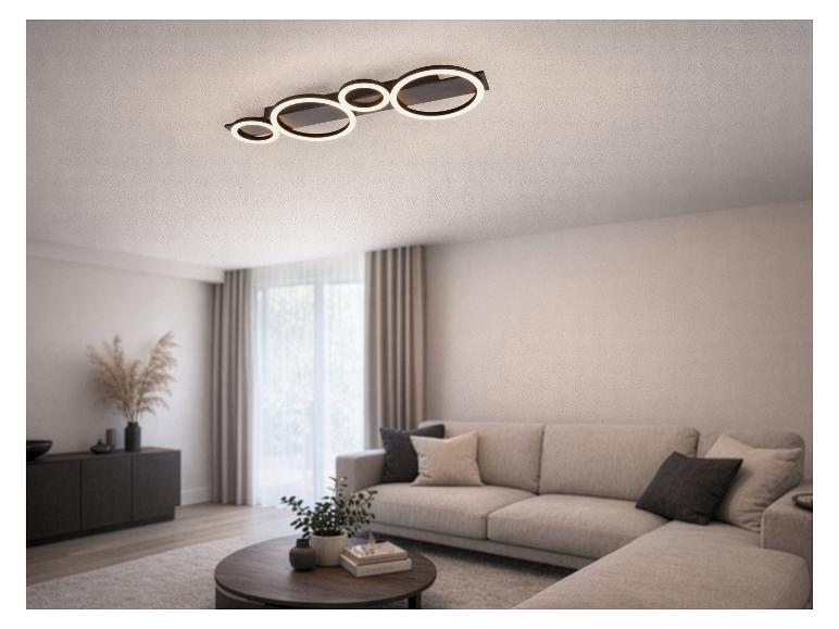 Moderne LED-Deckenleuchte mit beleuchteten Ringen in einem Wohnzimmer mit Sofa und Couchtisch.