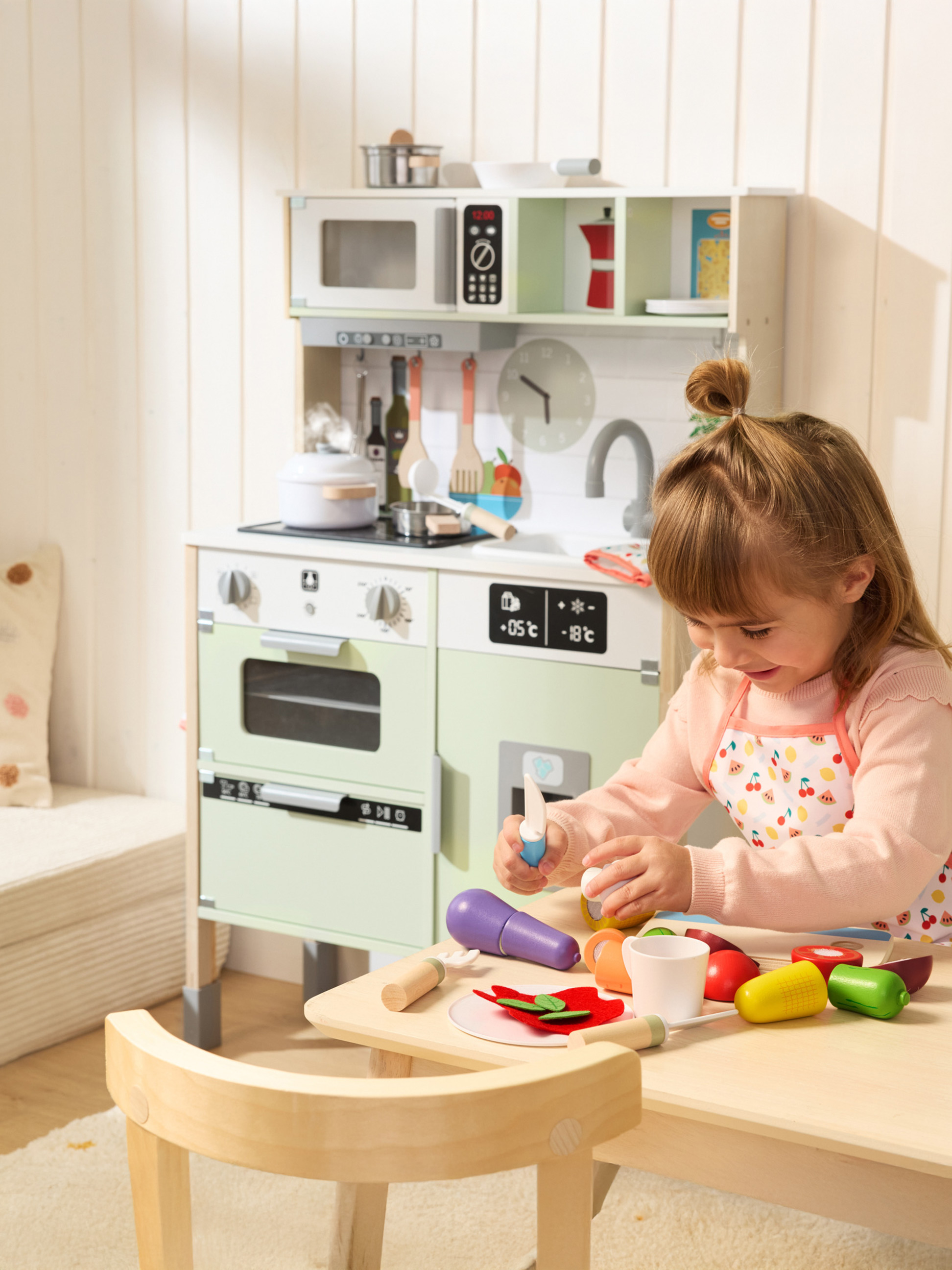 Mädchen spielt mit einer Spielküche aus Holz und Kochzubehör.