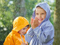 Zwei Kinder in Regenjacken, eines in blau, eines in gelb, spielen im Regen.