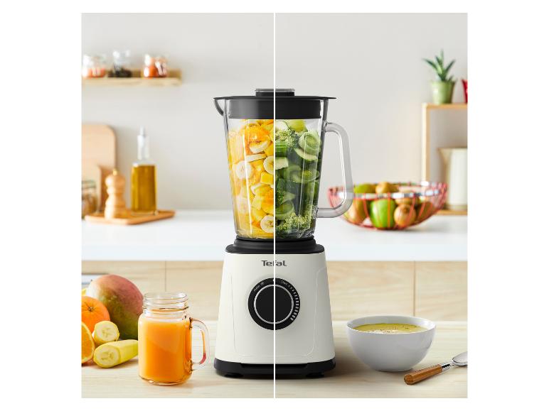 Mixer mit Obst und Gemüse, daneben ein Glas Saft und eine Schüssel Suppe.