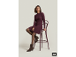 Frau in lila Strickkleid, Strumpfhose und braunen Stiefeletten sitzt auf einem Barhocker