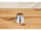 Mokakanne gefüllt mit gemahlenem Kaffee, Kaffeebohnen und einem Löffel auf einem Holztisch.